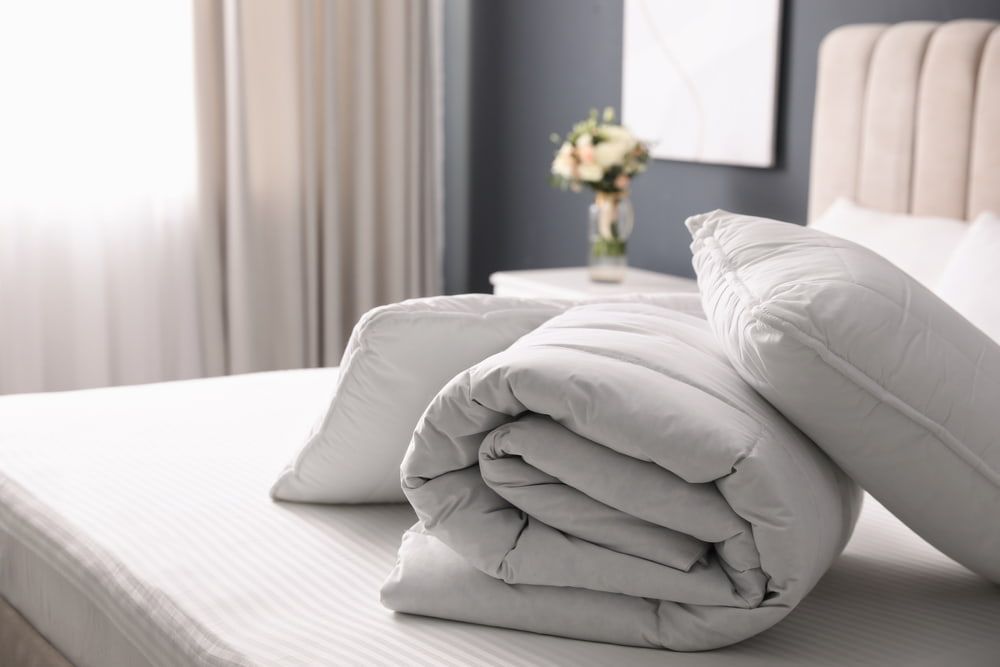 Bed with white bedding, two pillows, and a rolled-up blanket in a bedroom.