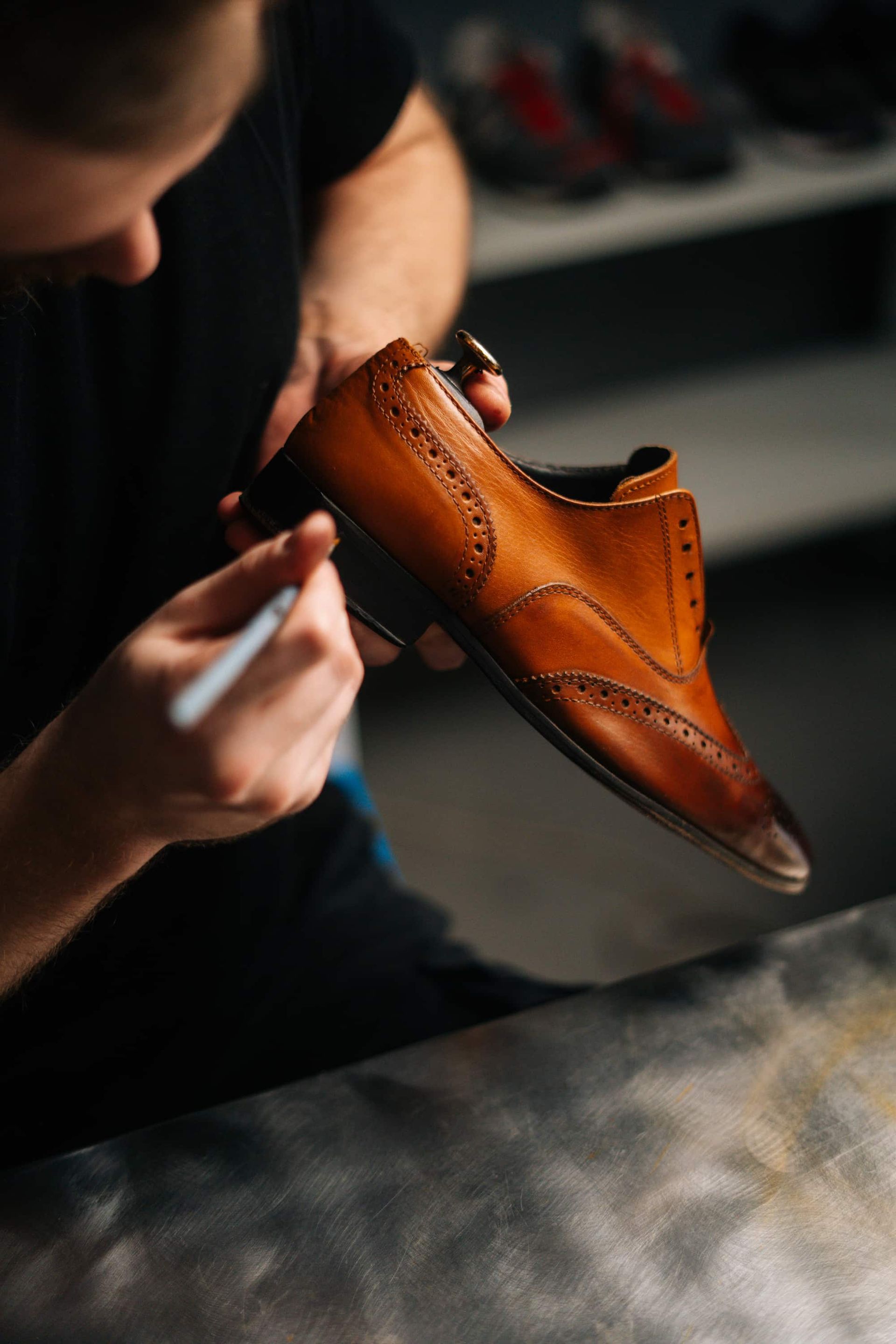 Person painting a brown leather shoe with a fine brush in a workshop.