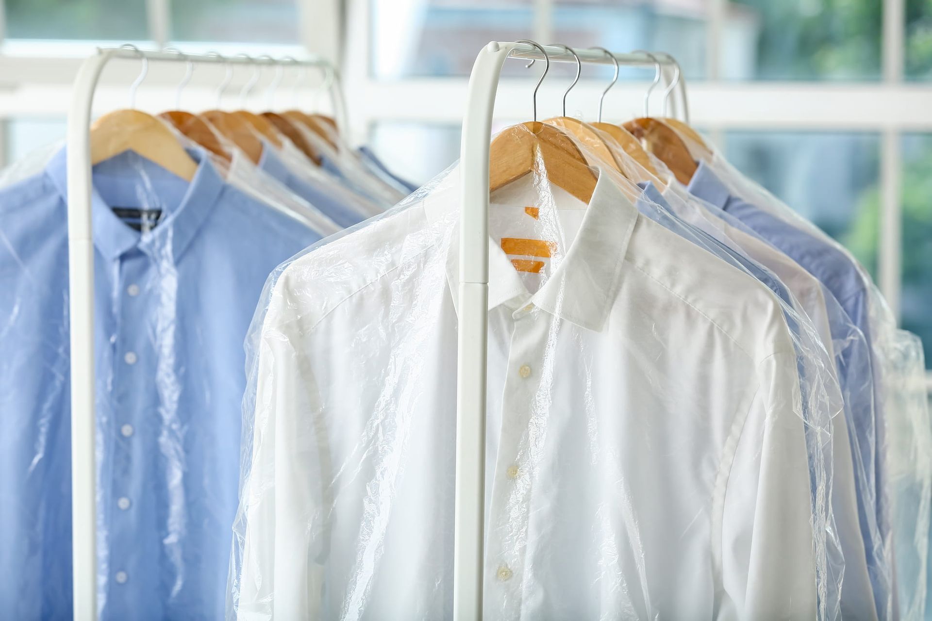 Shirts in plastic dry cleaning bags hang on a metal rack.