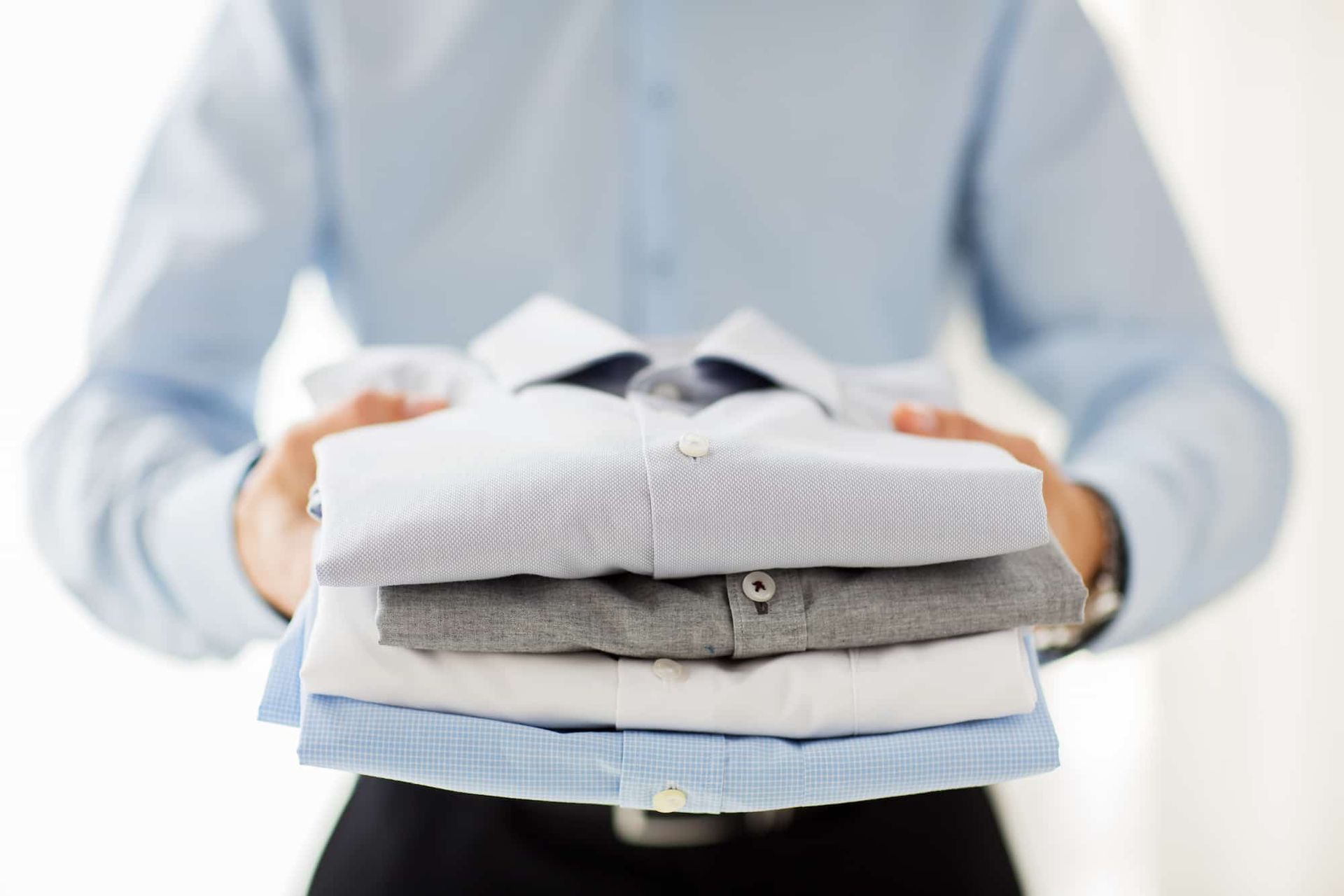 Person holding a stack of neatly folded shirts in various colors.