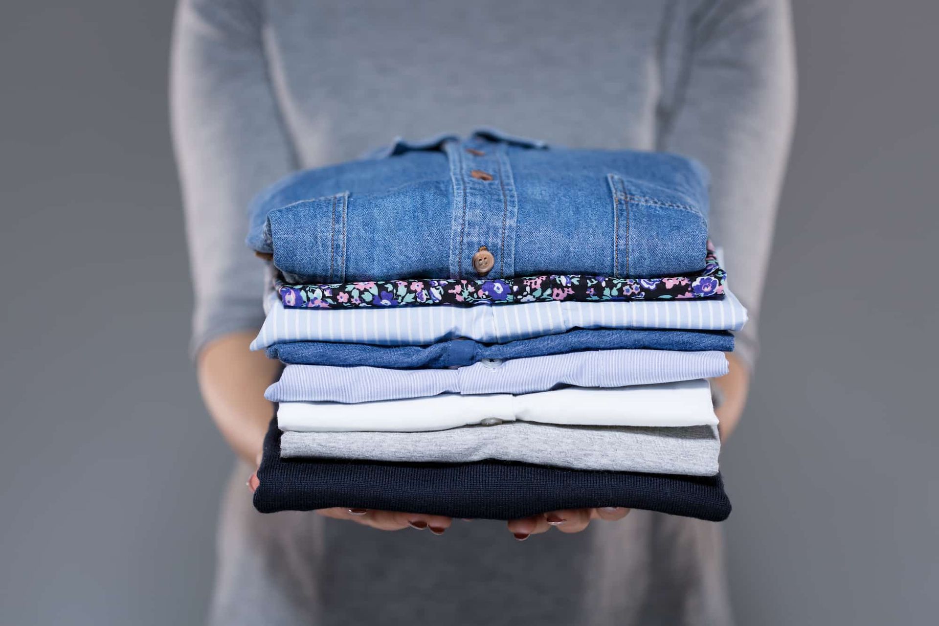 Person holding a stack of neatly folded clothing in various colors.
