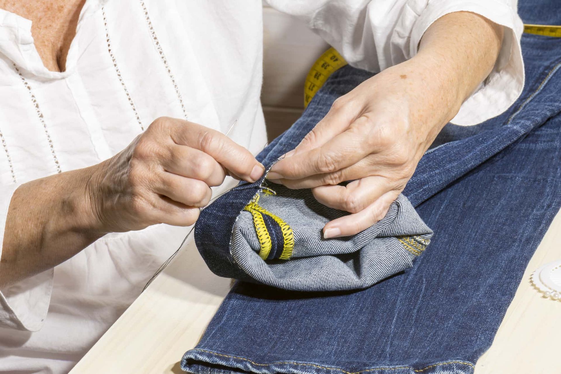 Hands of a person sewing the cuff of a blue jean.