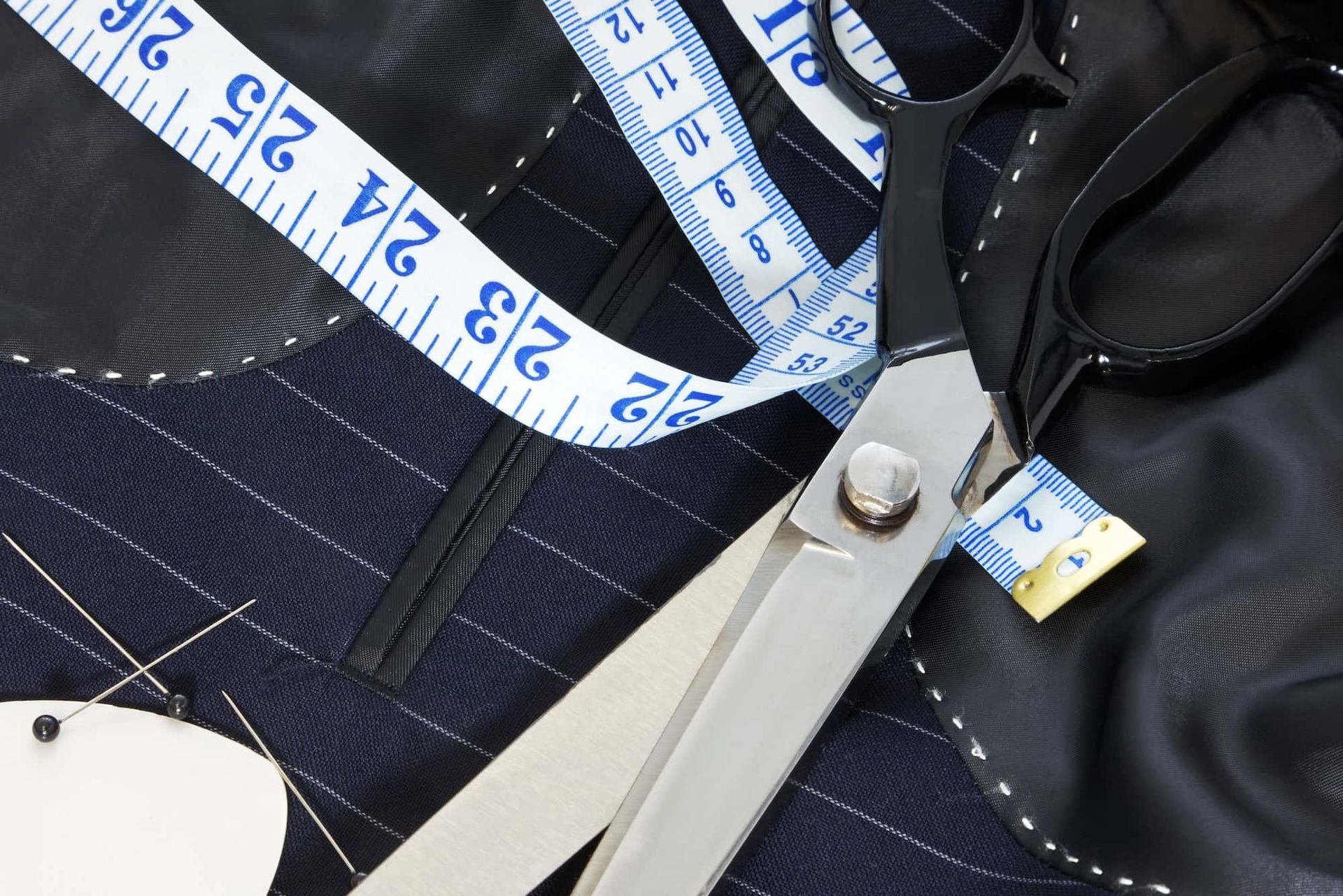 Scissors, measuring tape, and a garment on a tailoring table; tools for sewing.