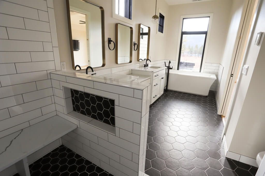 A bathroom with two sinks , two mirrors , a tub and a bench.
