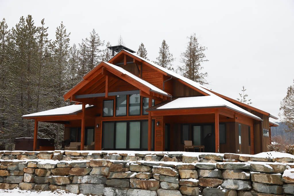 A large wooden house with a stone wall in front of it in the snow.