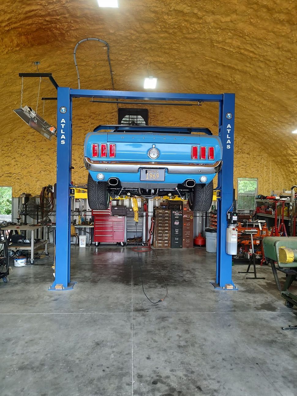 A blue mustang is on a lift in a garage.
