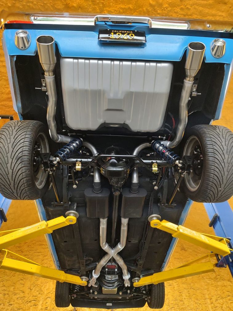 Undercarriage view of a car on a lift, showcasing a custom dual exhaust system with an X-pipe, painted black and silver.