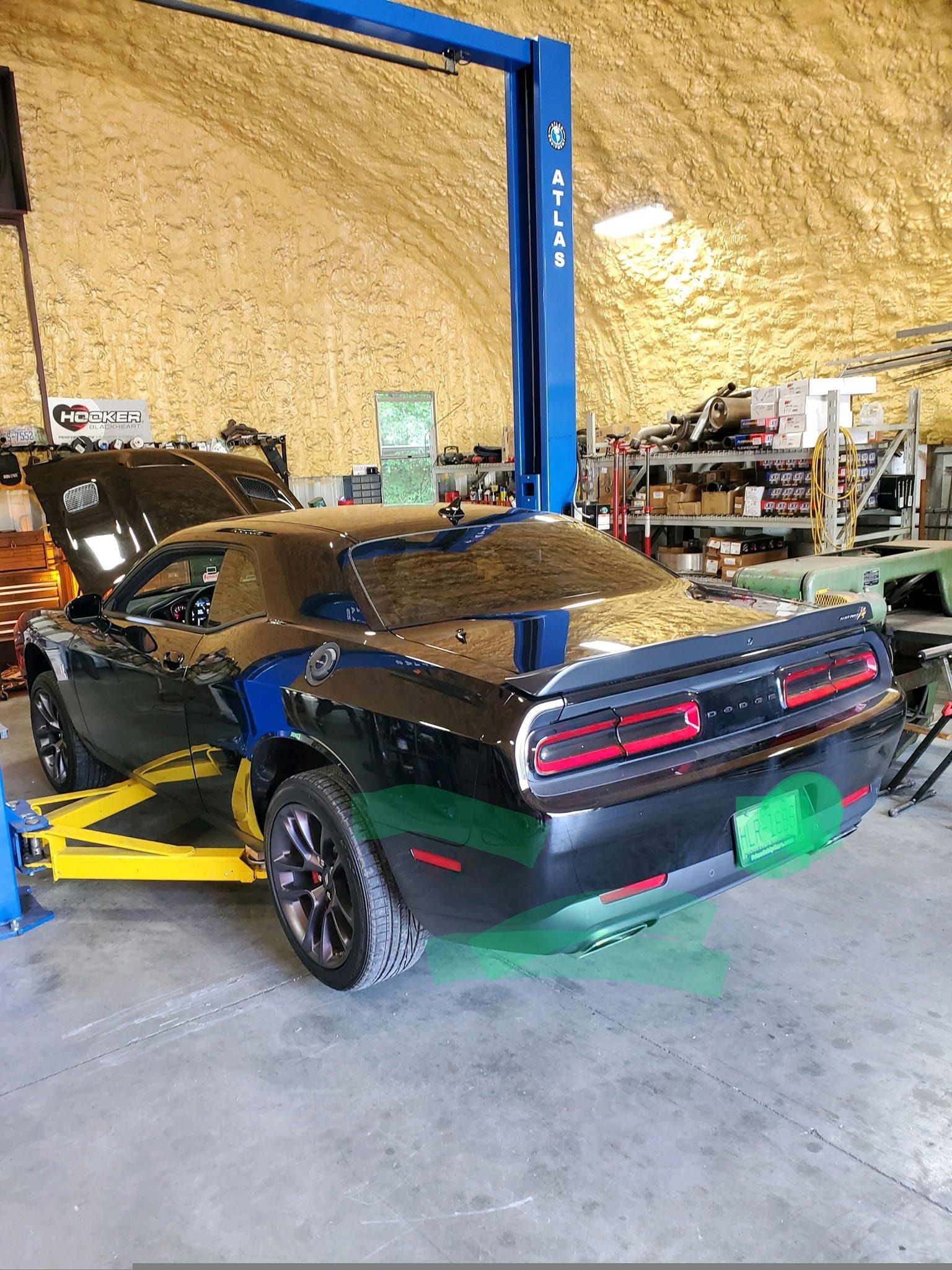 Black Dodge Challenger car on a yellow lift inside a garage, hood open.