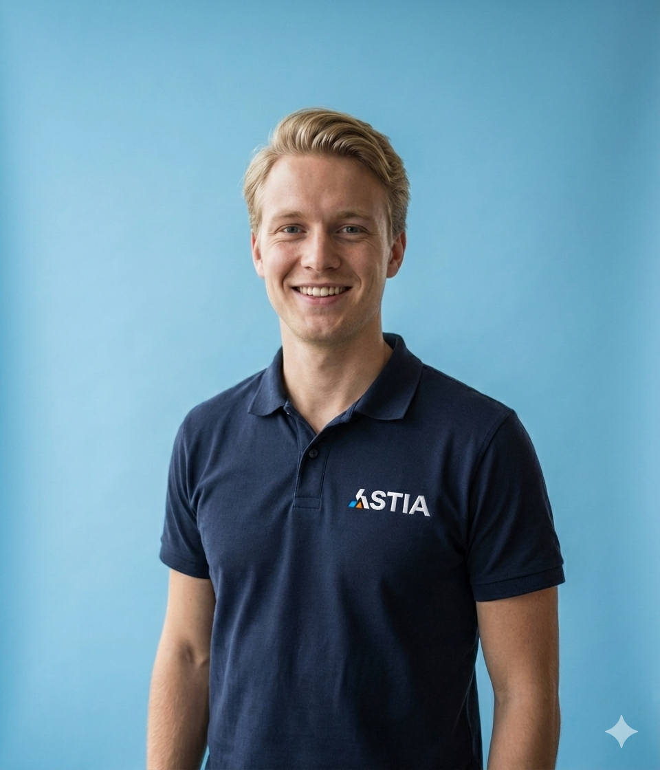 Blonde man in een donkerblauw poloshirt met bedrijfslogo, lachend tegen een blauwe achtergrond.