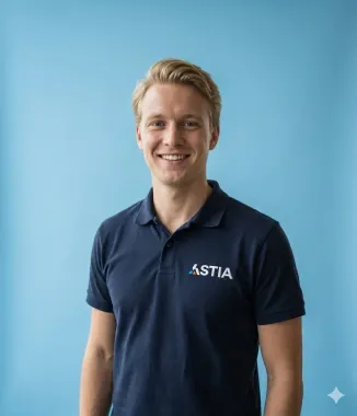 Een blonde man in een blauw poloshirt staat lachend tegen een lichtblauwe achtergrond, met het