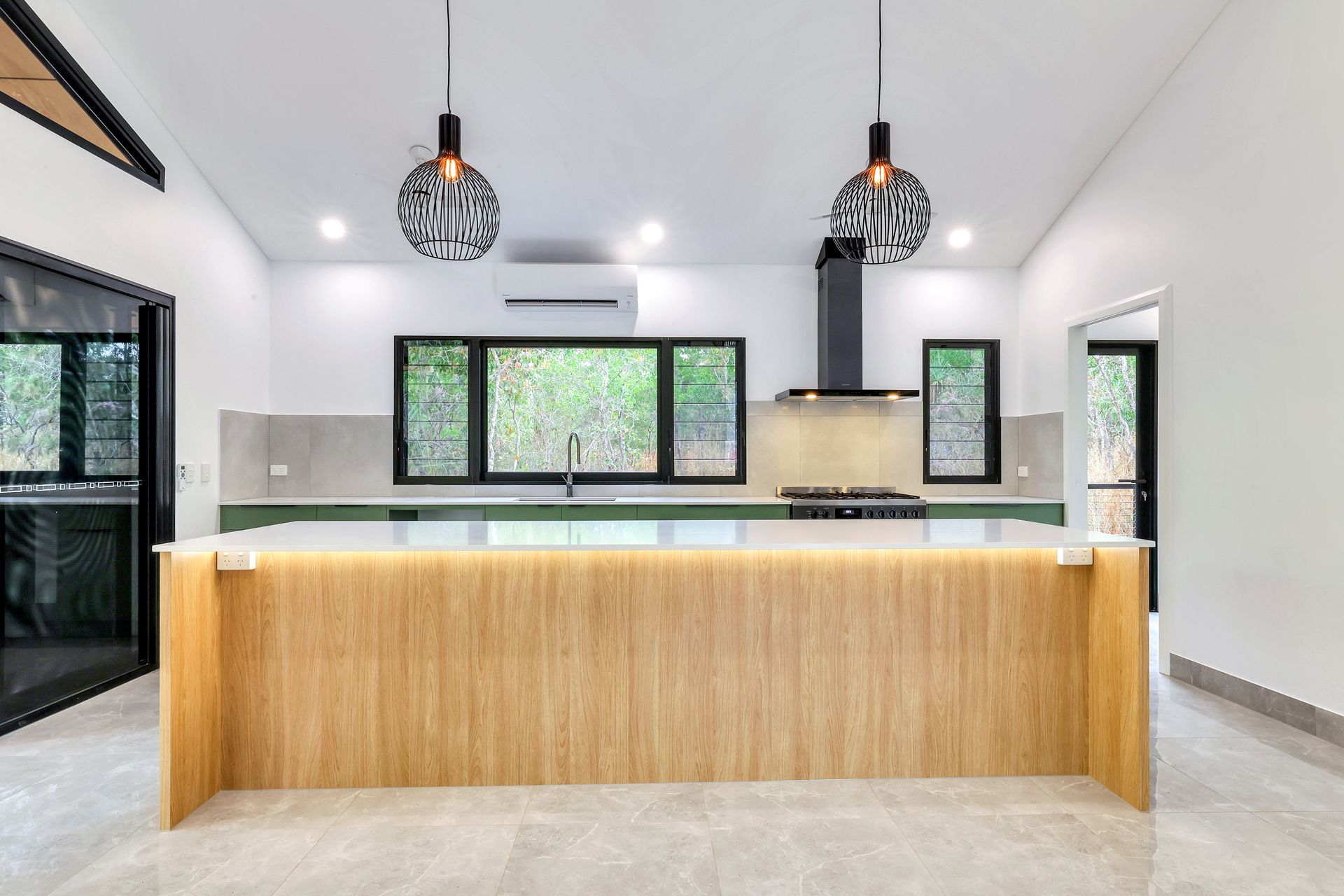 Modern kitchen with wood island, black range hood, and pendant lights. Green countertops and windows overlooking foliage — RMB Air Conditioning & Electrical in Winnellie, NT