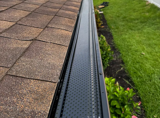 Plastic guard over new dark grey plastic rain gutter on asphalt shingles roof at shallow depth of field. 