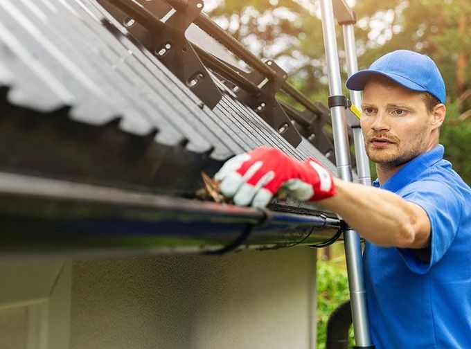 worker cleaning house gutter from leaves and dirt 
