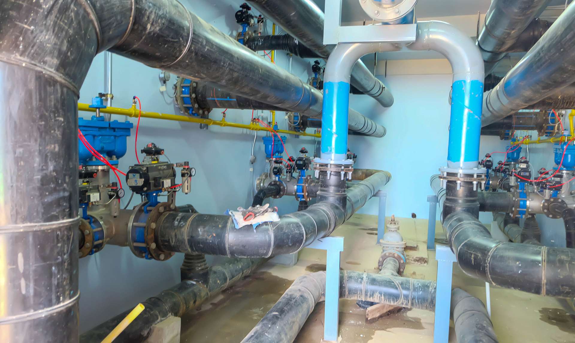 Piping system with black and blue pipes, valves, and gauges in an industrial setting.