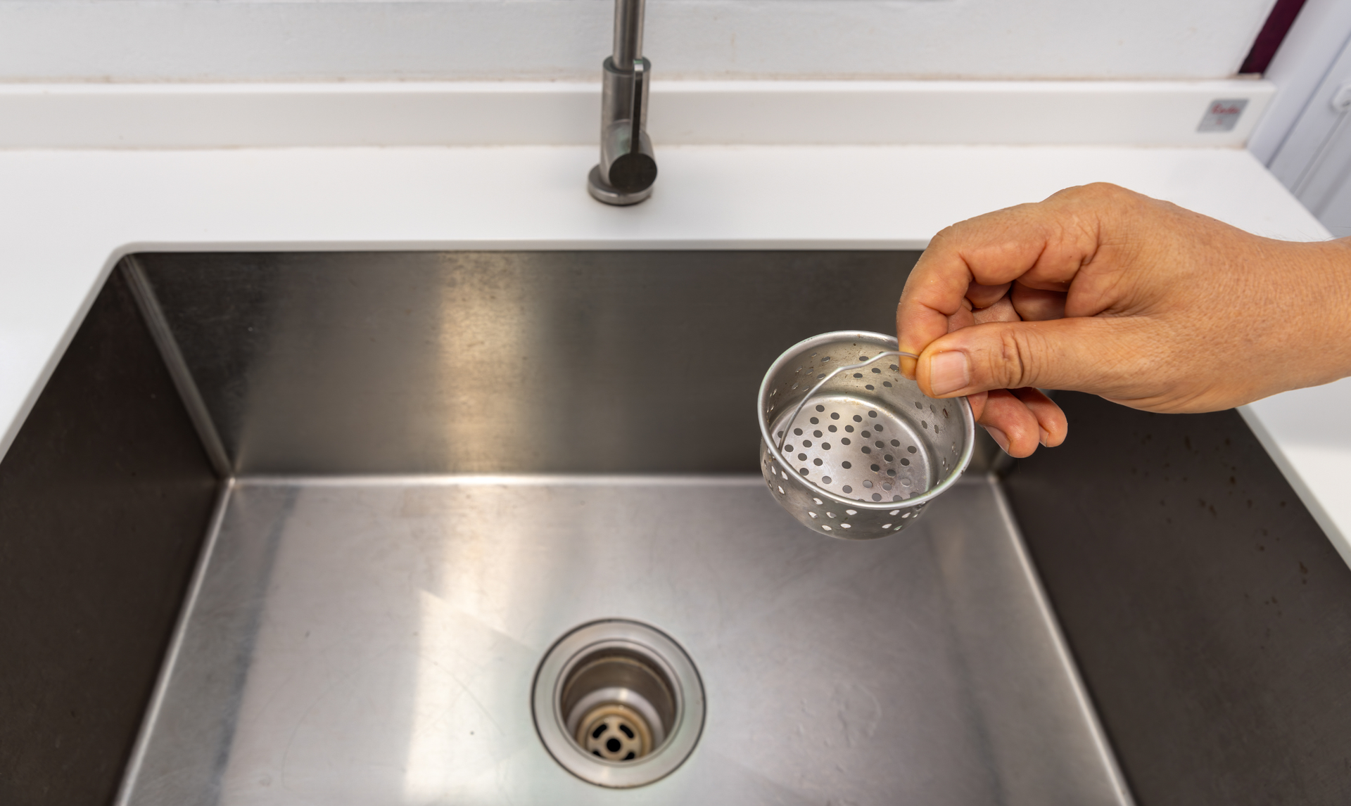 Hand holding strainer over a stainless steel sink, near a faucet.