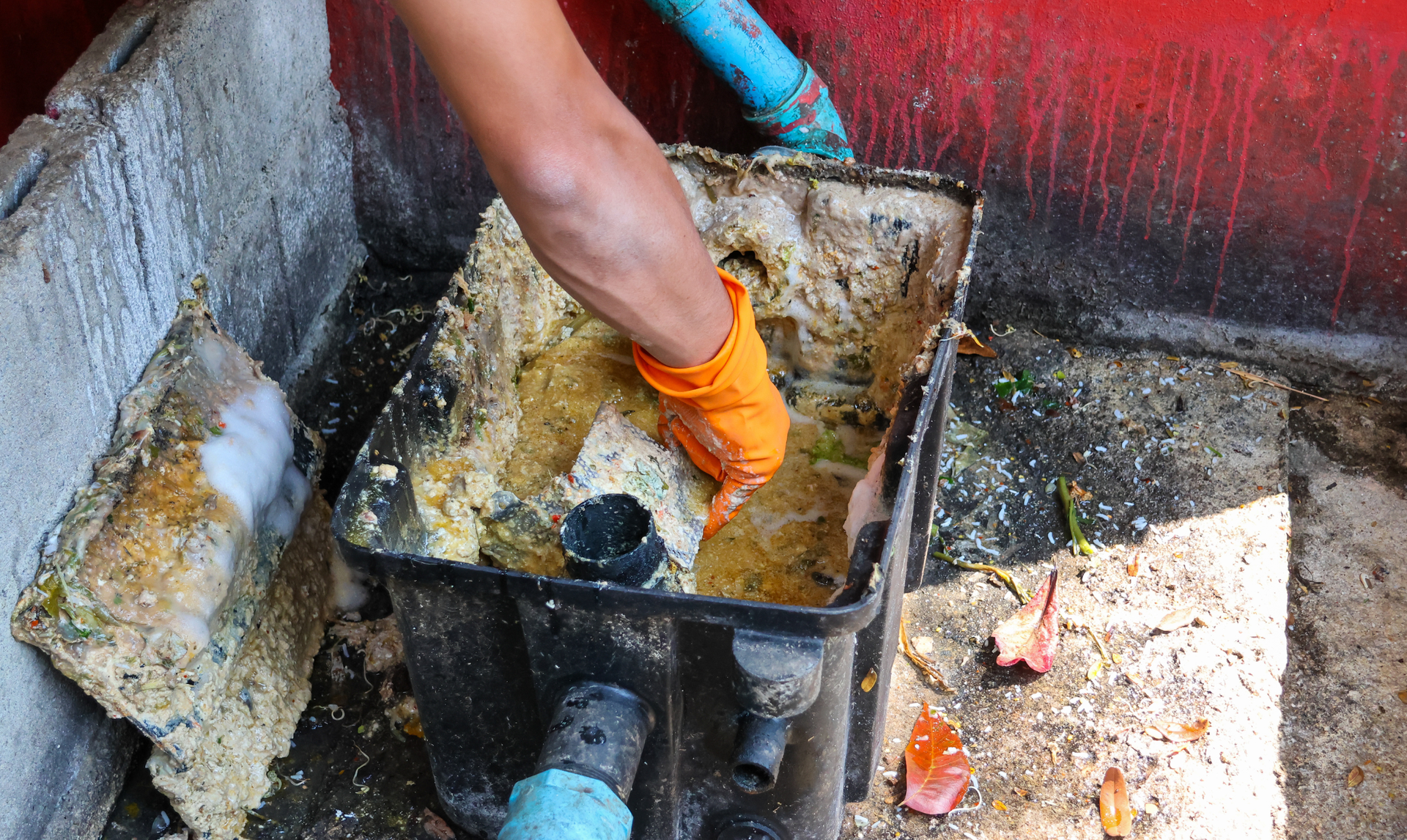 Person wearing orange gloves cleaning a greasy, clogged filter box.