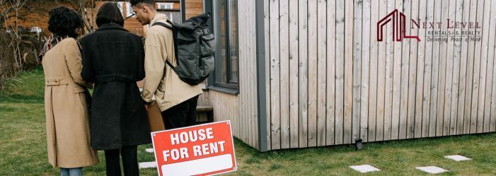 An image of three people standing next to a house with a house for rent sign infront of it.