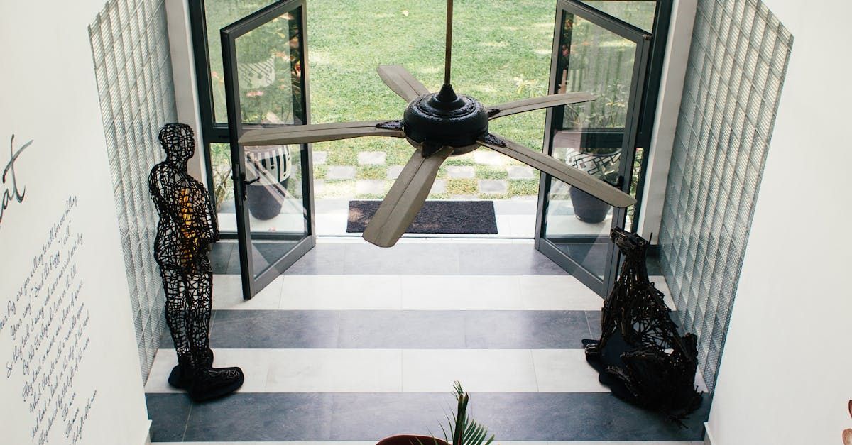 A doorway with a black and white striped floor, flanked by sculptures. A ceiling fan hangs above.