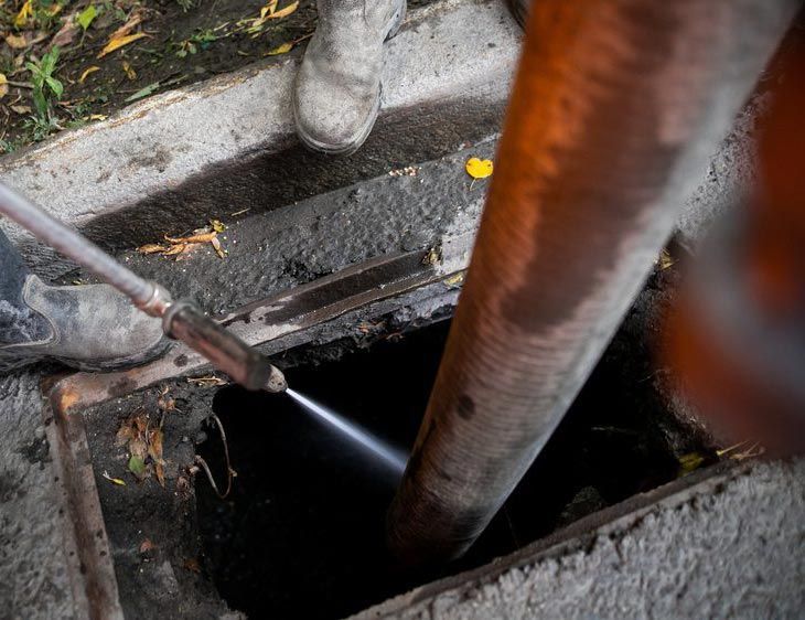 A person is using a high pressure washer to clean a drain.