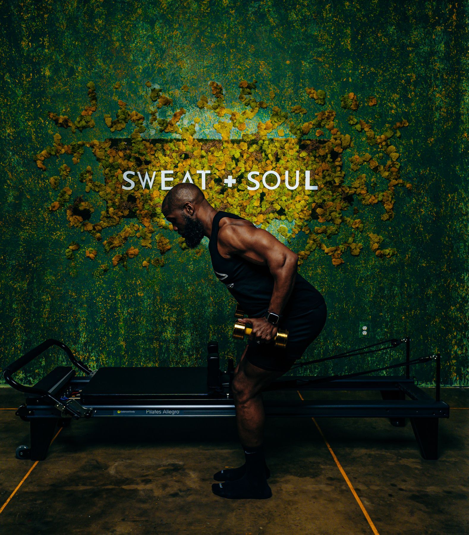 A man is lifting a dumbbell in front of a sign that says sweat + soul