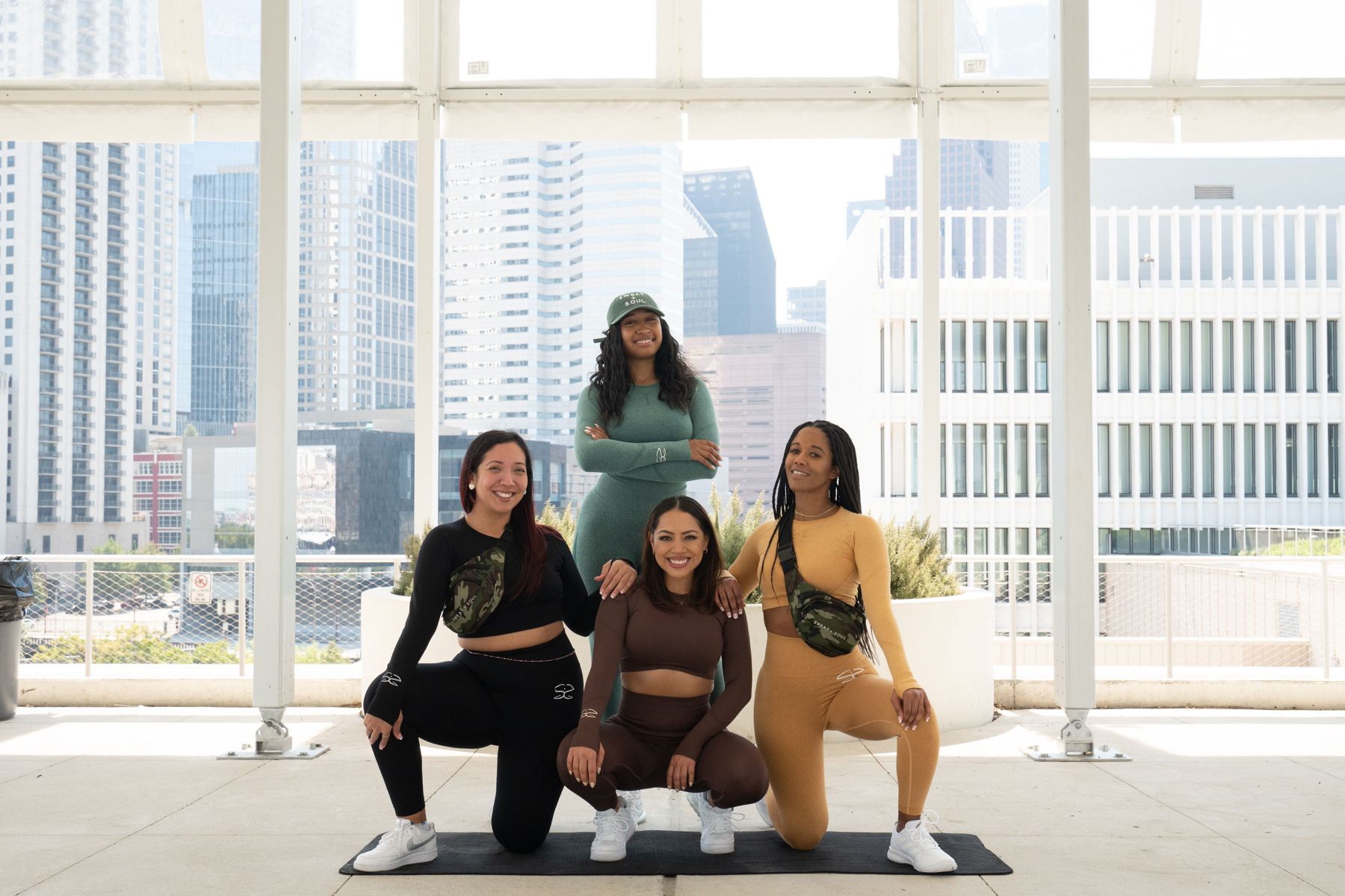 A group of women are squatting on a yoga mat in front of a window.