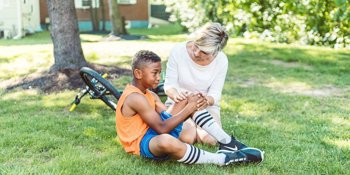 Adult helping child adjust a prosthetic leg while sitting on grass in a park