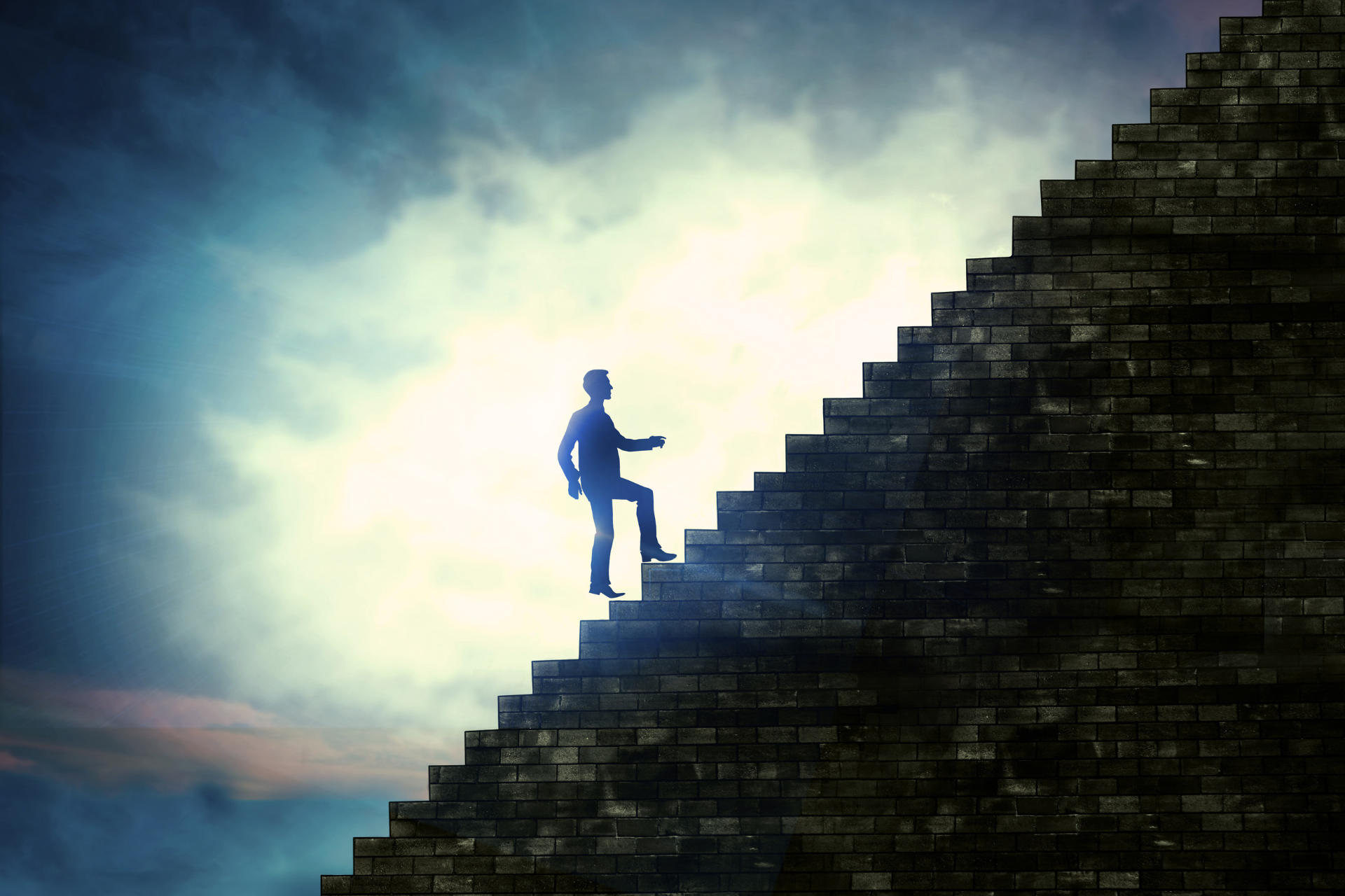 Silhouette of a person climbing a tall stone staircase towards a bright light in a cloudy sky.