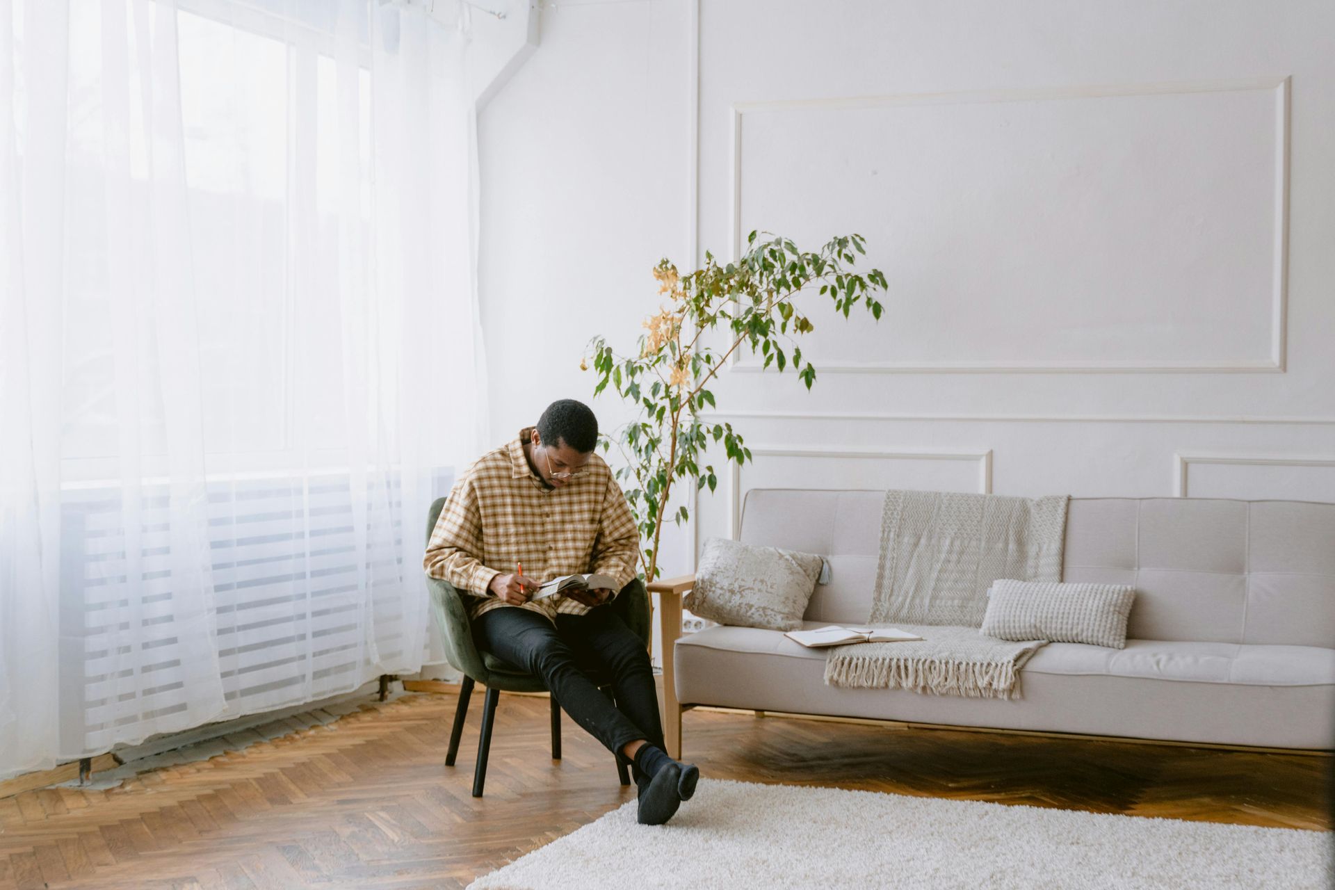 A man is sitting in a chair reading a book in a living room.