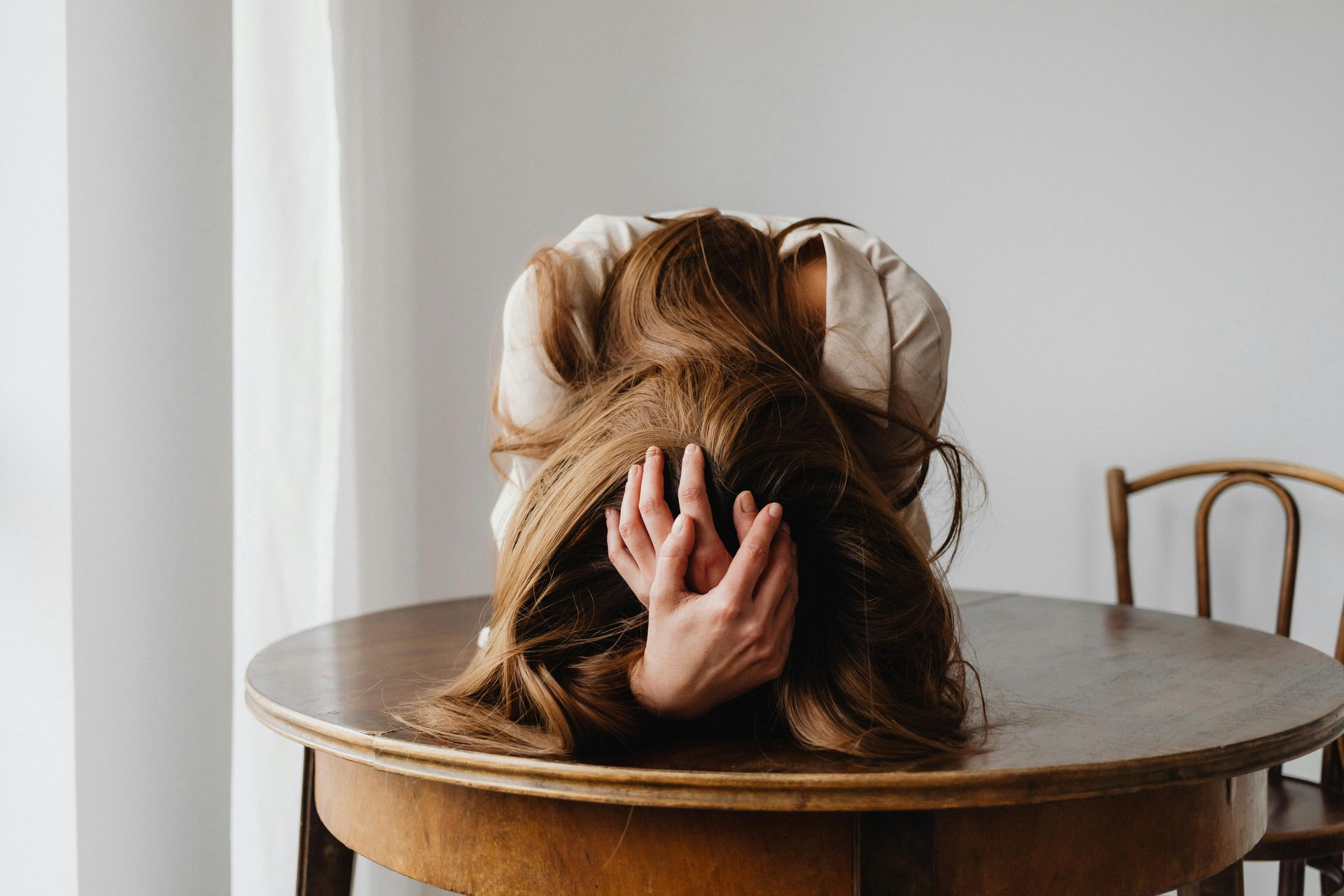 A woman is sitting at a table with her head in her hands.