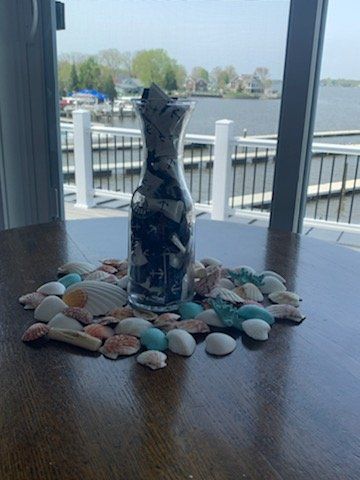 A vase filled with seashells is sitting on a table next to a window.