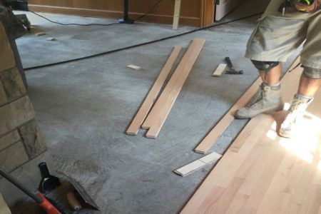A man is working on a wooden floor with a hammer.