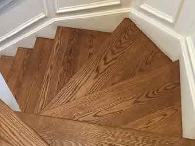 A close up of a wooden spiral staircase with white trim.