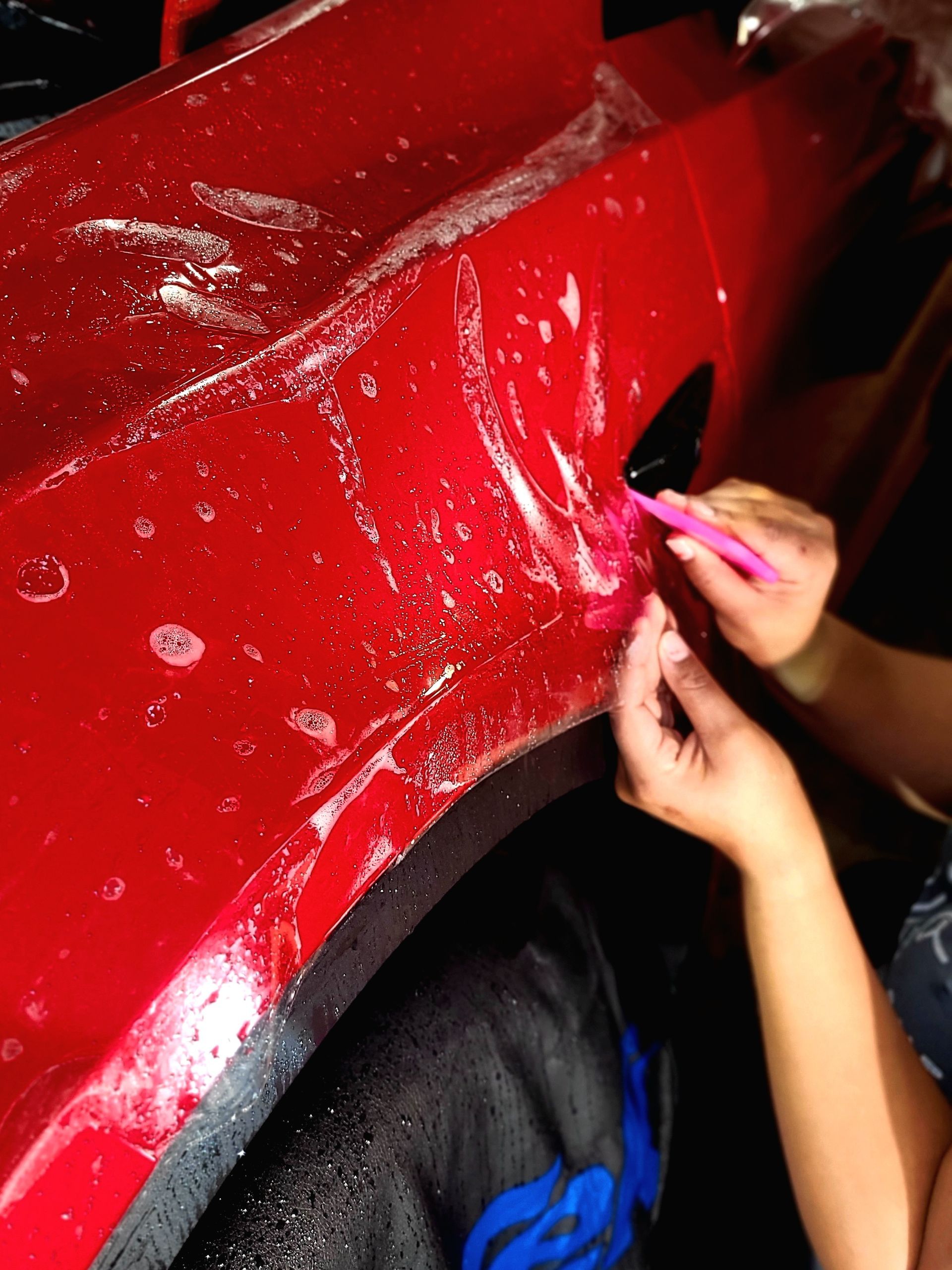 A person is cleaning a red car with a pink brush