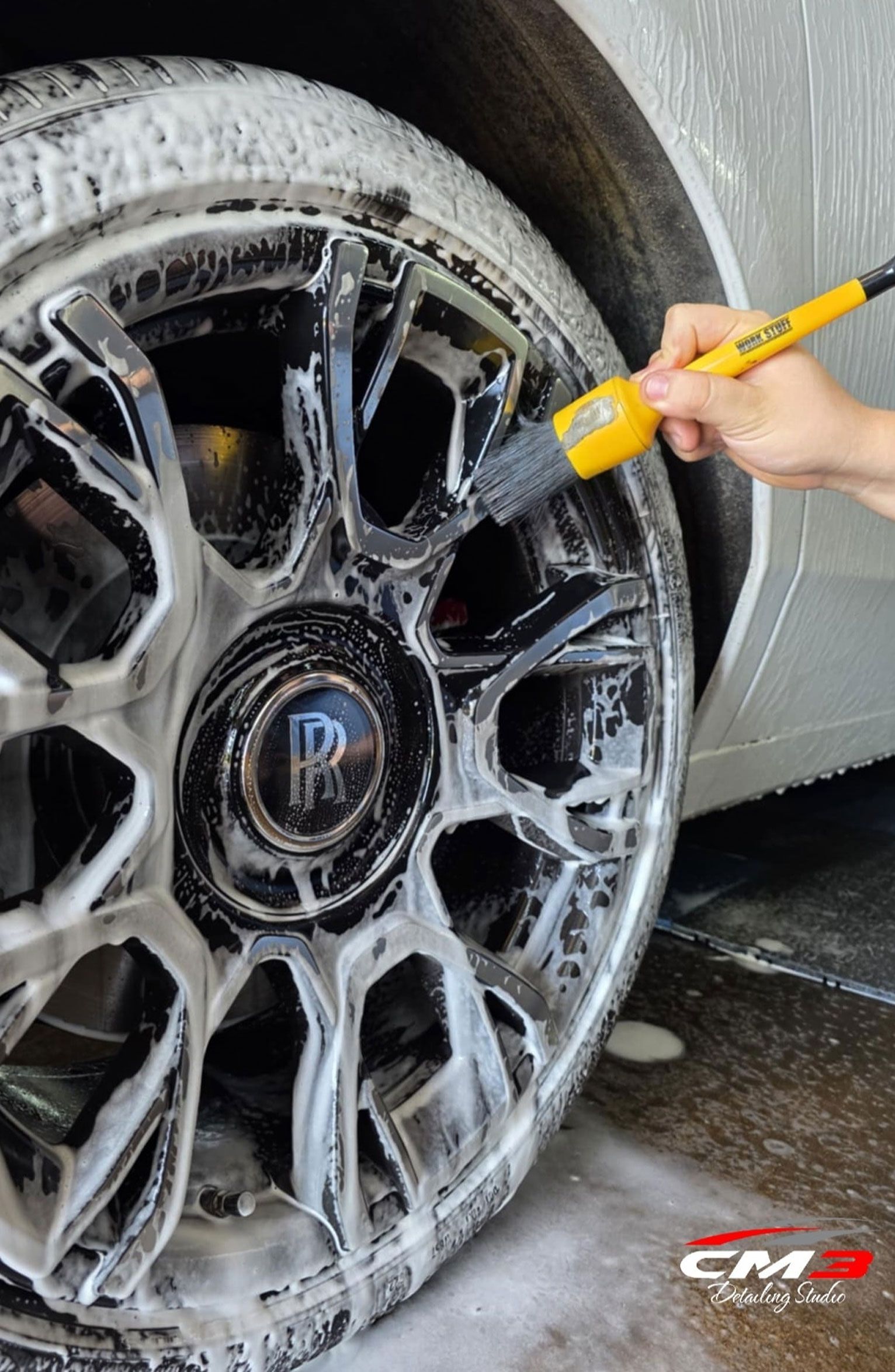Cleaning a car wheel with a brush and soapy foam.
