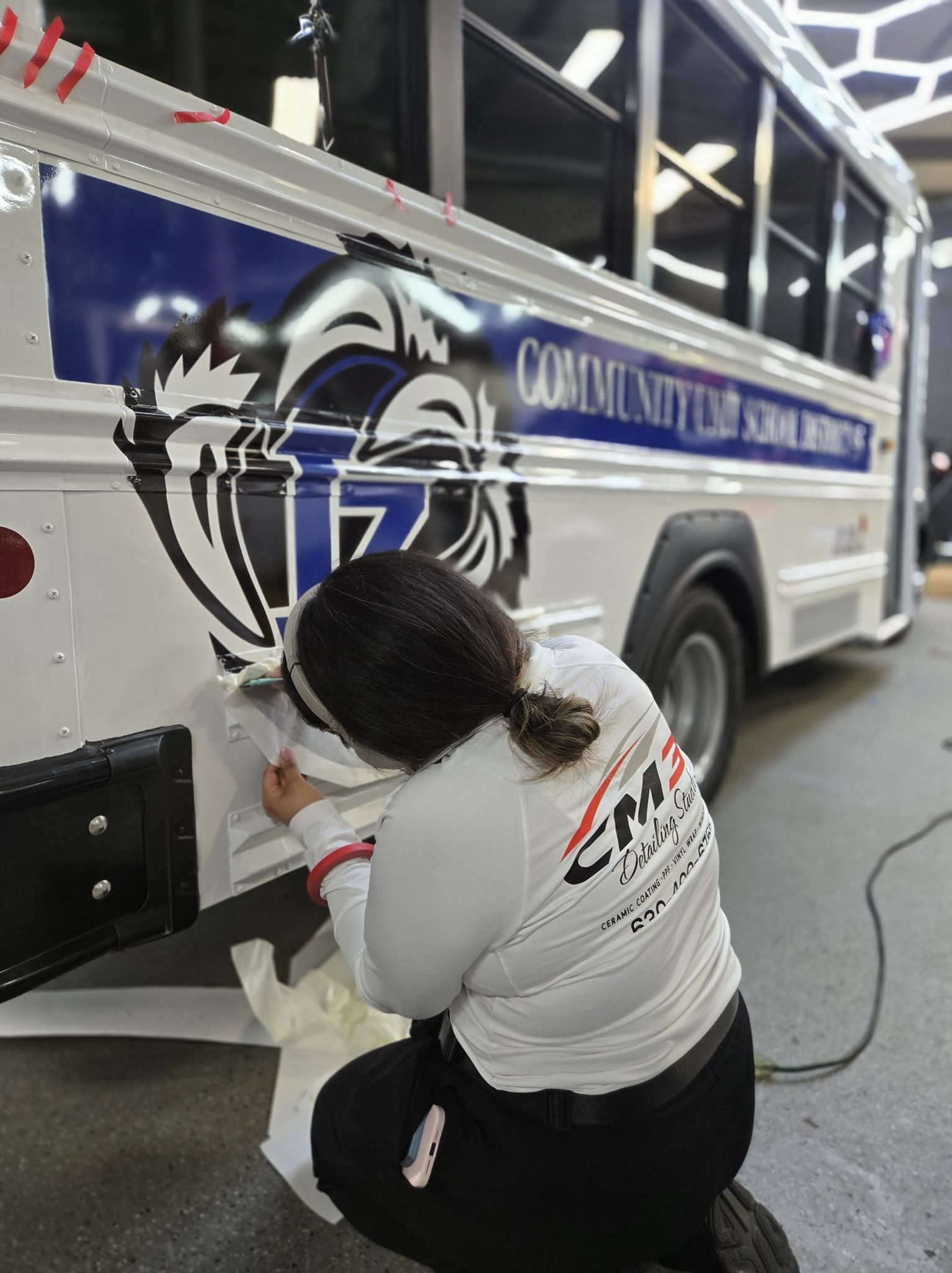 Person applying decal to a school bus. The bus is white with blue and black graphics.