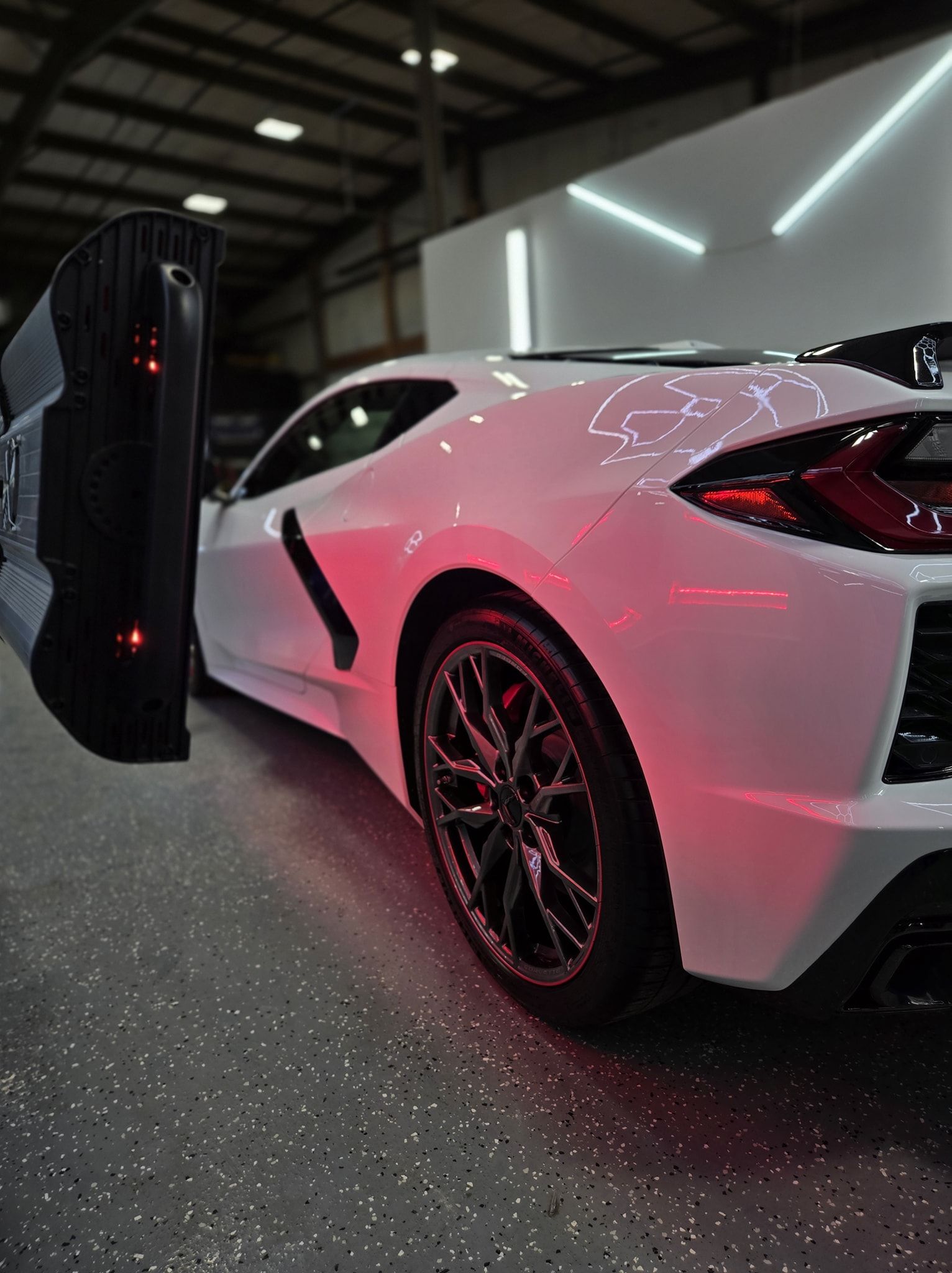 White sports car being scanned, red lights, indoor facility.