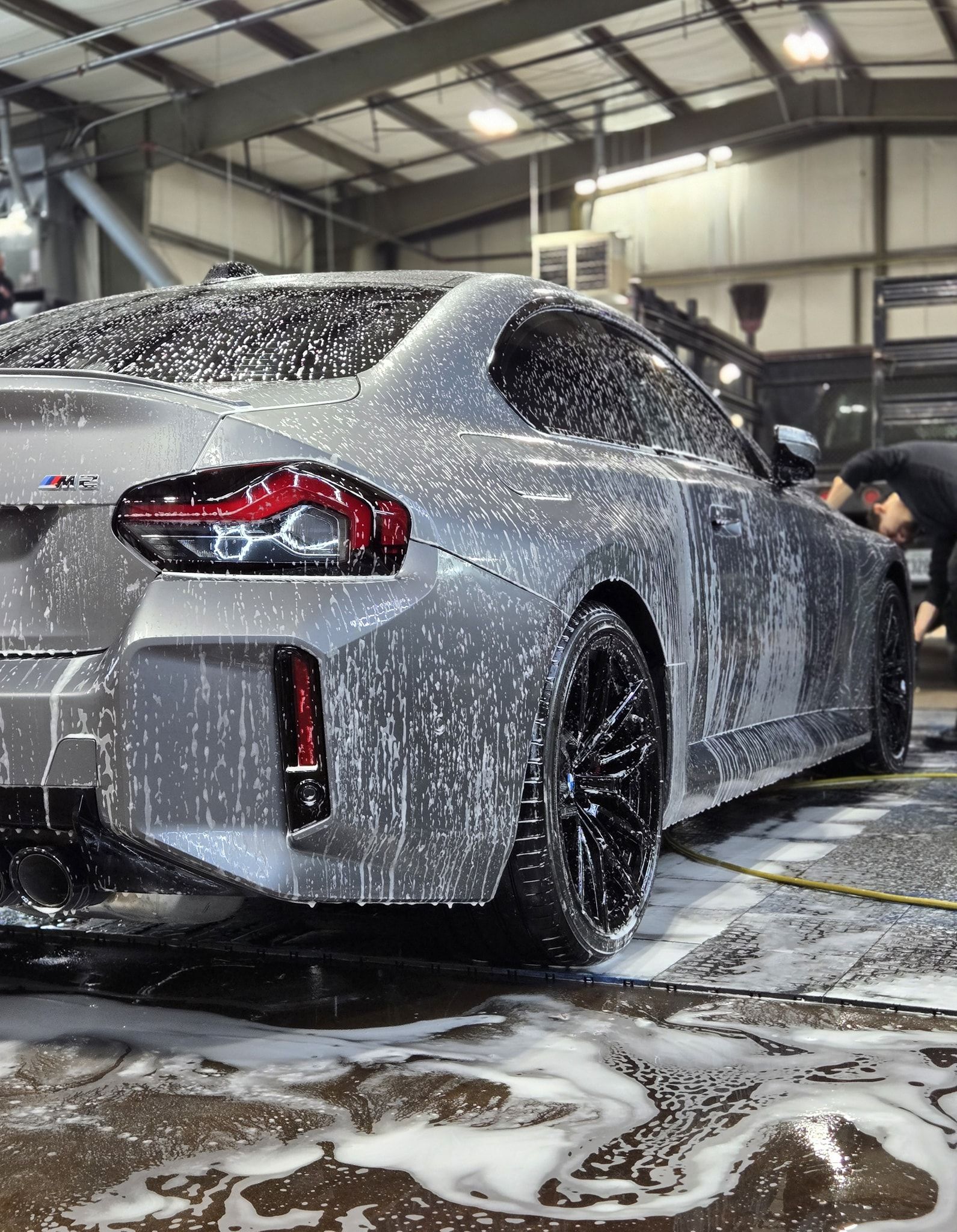 Gray sports car covered in foam being washed at a car wash facility.