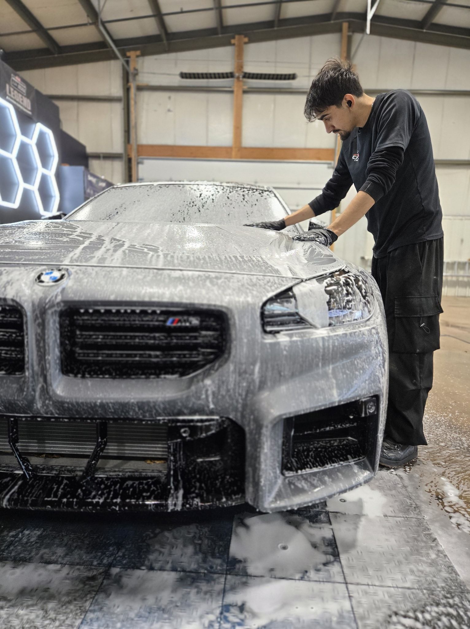 Person washing a gray BMW in a garage, covered in soap suds.