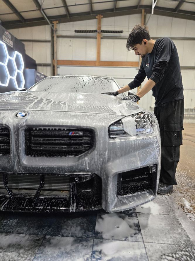 Person washing a gray BMW in a garage, covered in soap suds.