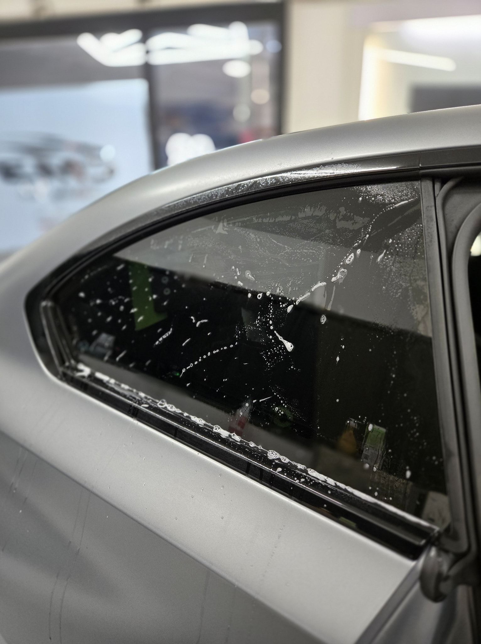 Car window with window tint being applied; the glass is wet with bubbles.