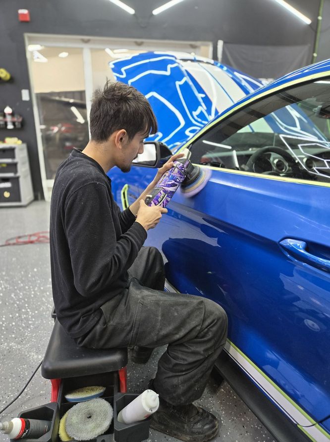 A person polishing a blue car with a machine in a workshop.