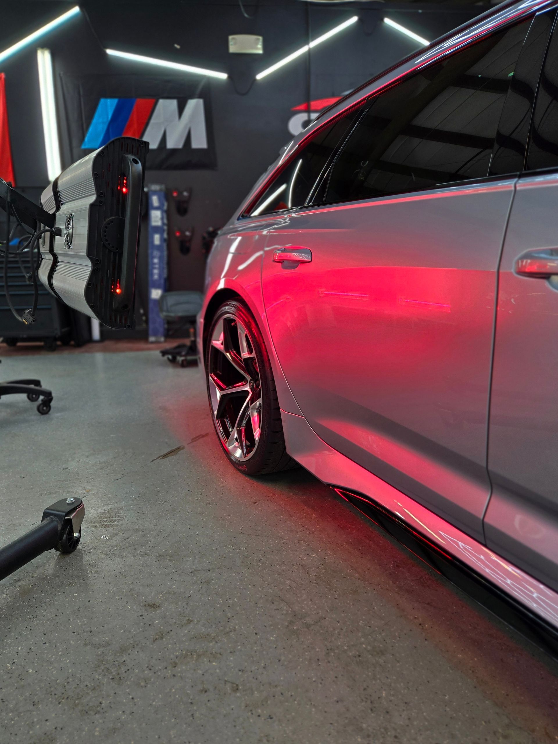 Silver car with red lighting in a garage, next to a BMW emblem.