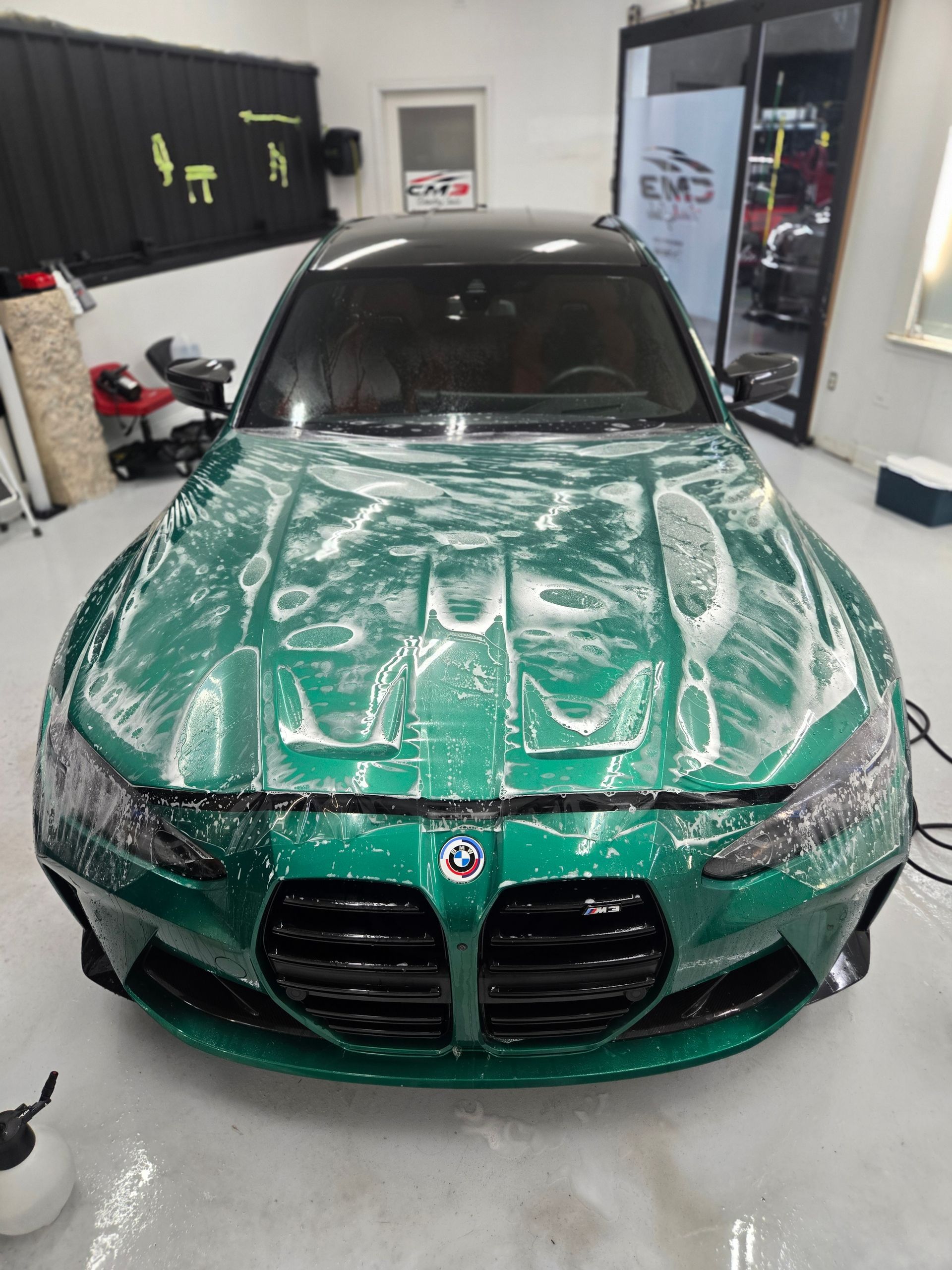 Green BMW M3 car covered in soapy foam, inside a garage.