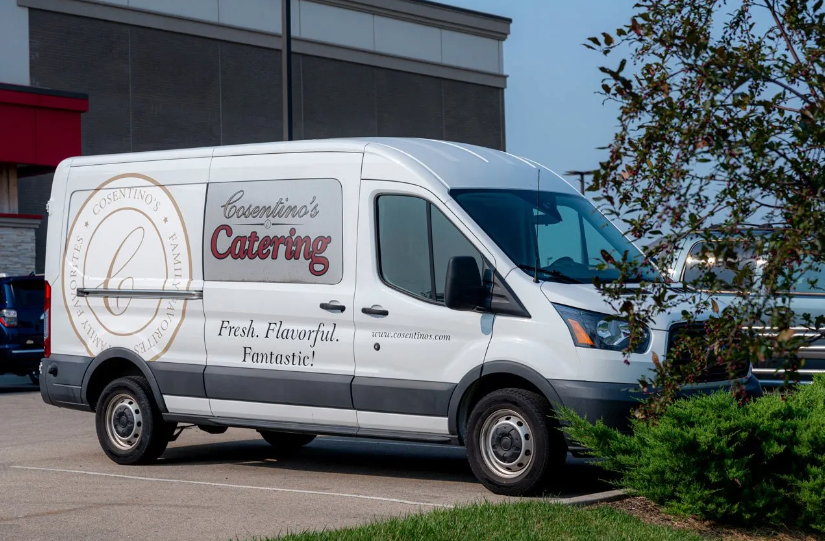 A white catering van is parked in a parking lot.