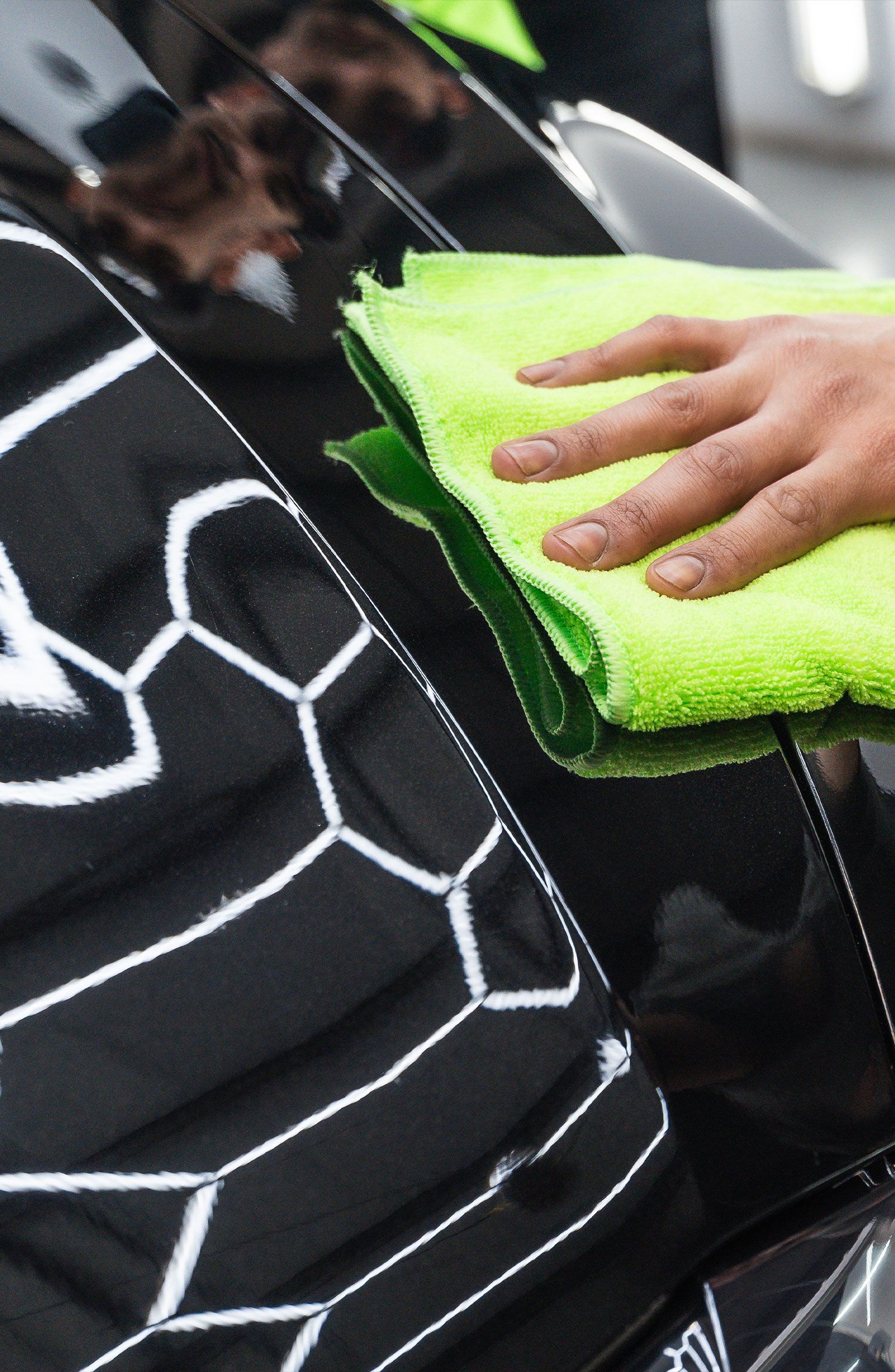 Hand wiping a shiny black car with a bright green microfiber cloth.