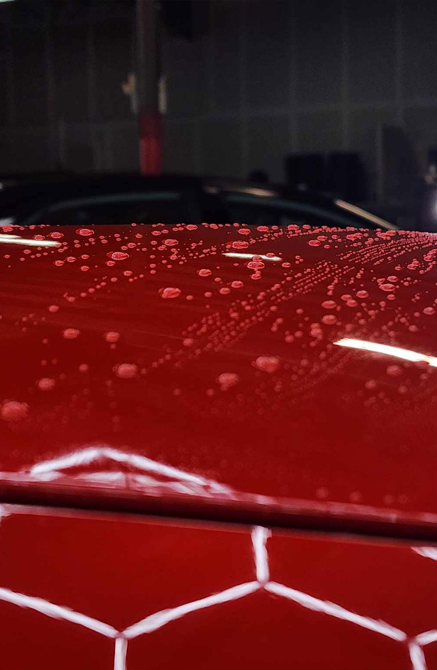 Red car hood with water beading, dark background, car in a shop.