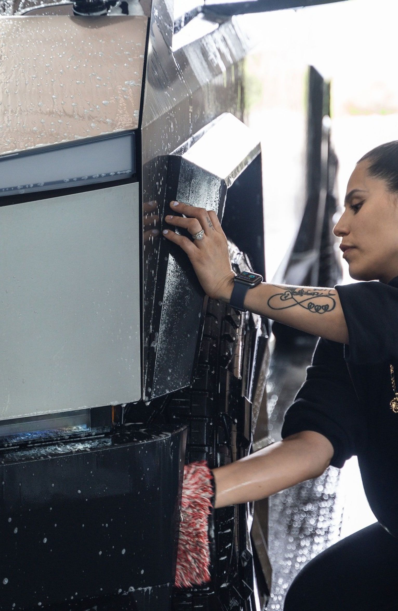 Person washing a black car, using a wet red mitt.