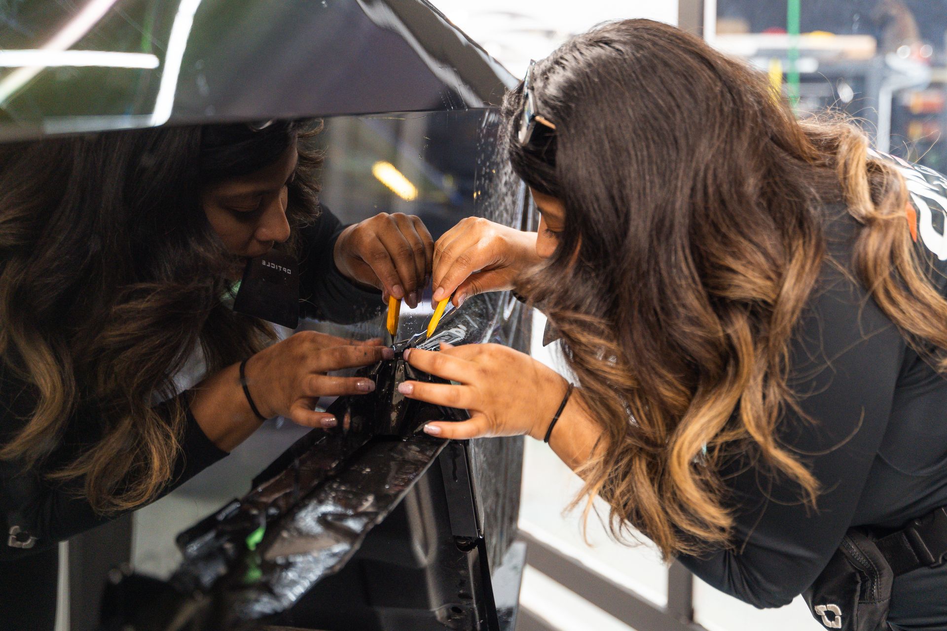 Woman applying tint film to a car window with a precision tool in a shop setting.
