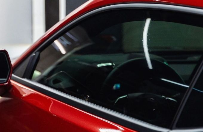 Close-up of a red sports car side window with a dark window tint applied professionally