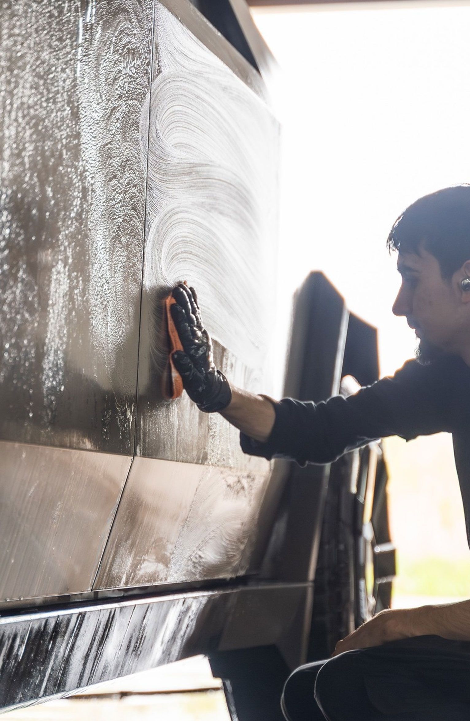 Person wearing gloves washes a vehicle with a sponge.